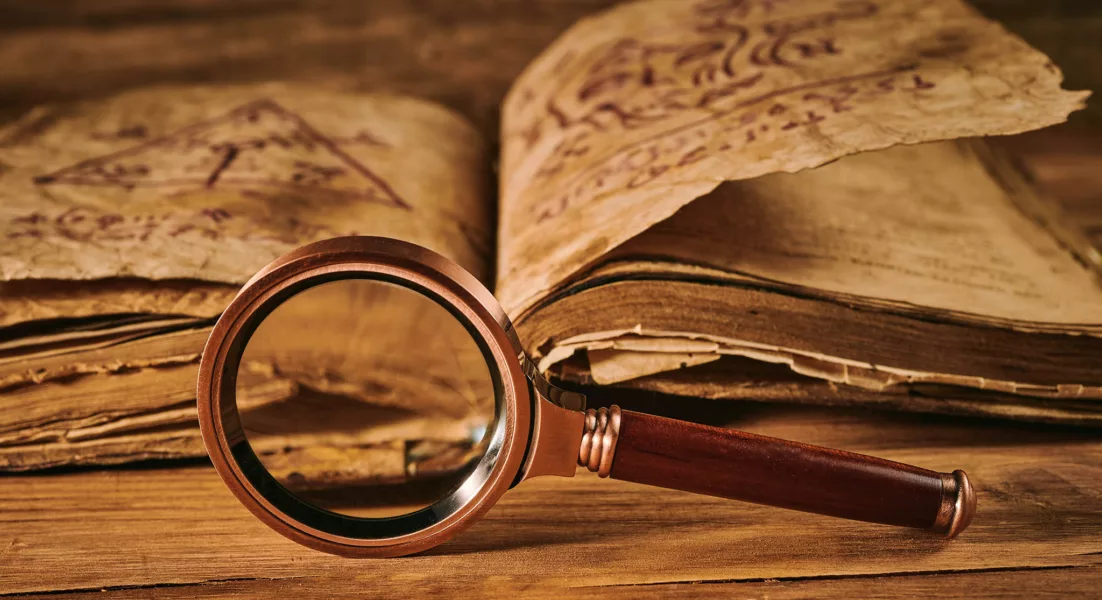 Magnifying glass and the ancient magic book on wooden table